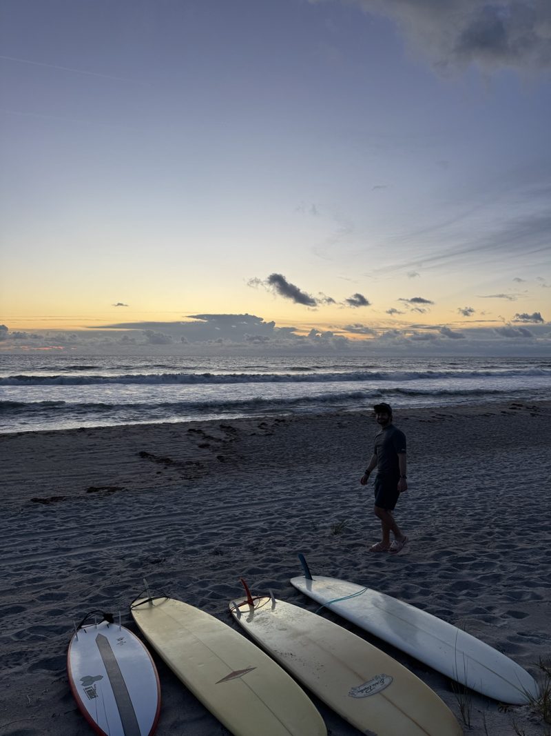 Surfboards on the sand and a club member beside the ocean at dawn