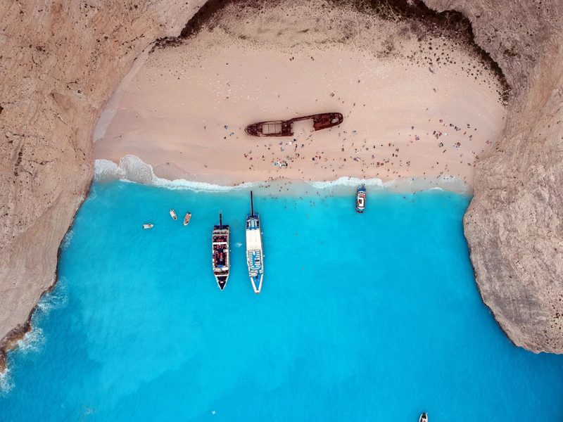 A shipwreck on a sandy beach enclosed by cliffs and bright blue water