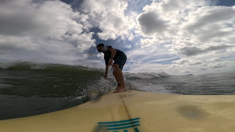 Tryfon riding a wave beneath a cloud-filled sky, photographed from his surfboard